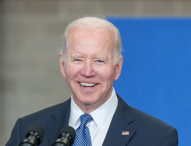 President Joe Biden smiles and points in a TikTok video, surrounded by young people and holding a football.