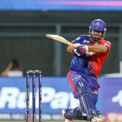 A photo of Rishabh Pant in his Delhi Capitals jersey, batting on the field. He is wearing a helmet and holding a cricket bat.