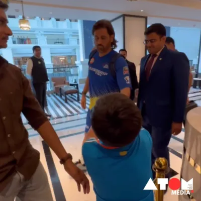 The image captures MS Dhoni signing a cap for a young fan, showcasing a heartwarming interaction between the cricket star and his admirer.