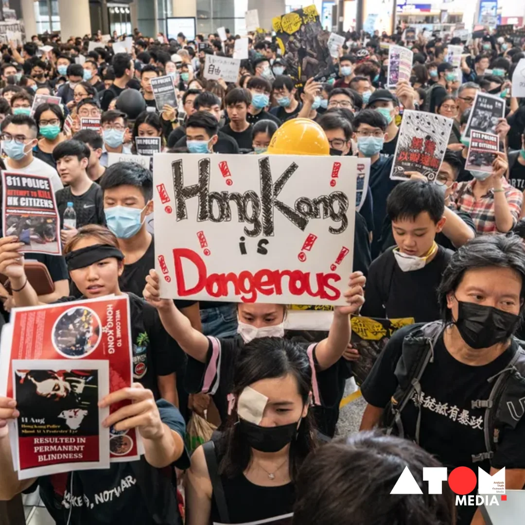 Protesters hold banners and flags during a rally in Hong Kong, with police officers visible in the background.