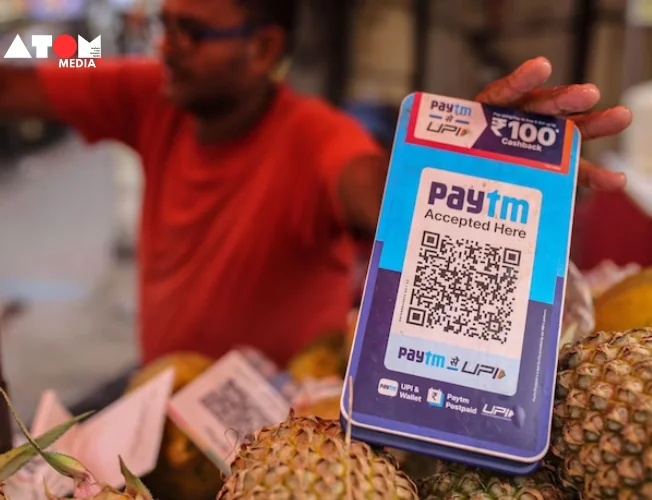 A smartphone displaying the Paytm app and a stock chart showing a sharp increase.