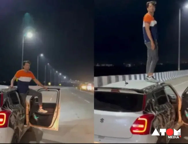 A white Maruti Swift car speeding down a road with a man standing dangerously on the roof.