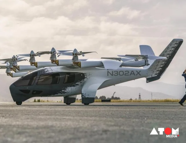 : A sleek, silver electric vertical takeoff and landing (eVTOL) aircraft with six rotors hovers near a modern cityscape in India.