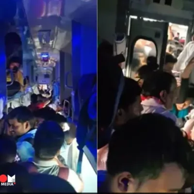 A crowded train compartment in India, with passengers sitting on luggage and overflowing aisles.